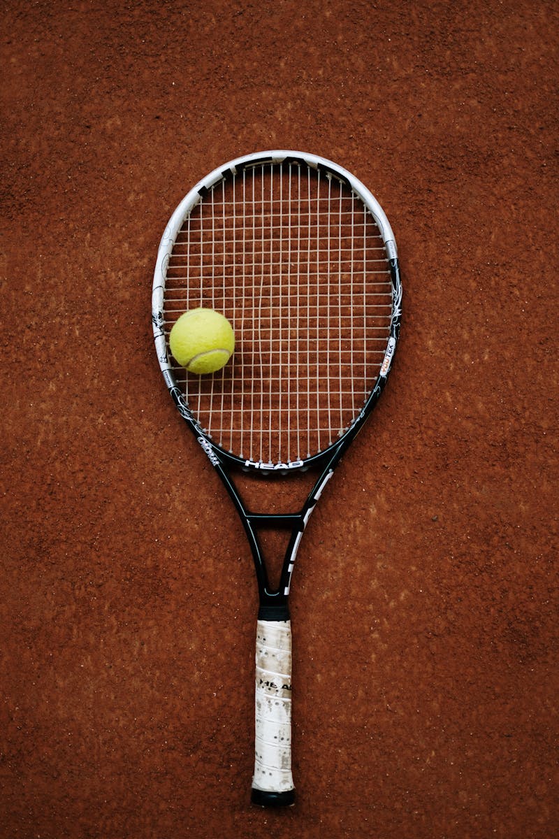 Close-up of a tennis racket and ball on a clay court, perfect for sports imagery.